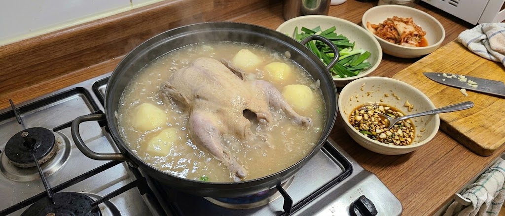 냄비 속 닭곰탕 국물이 맑게 끓는 장면 — 김이 피어오른다